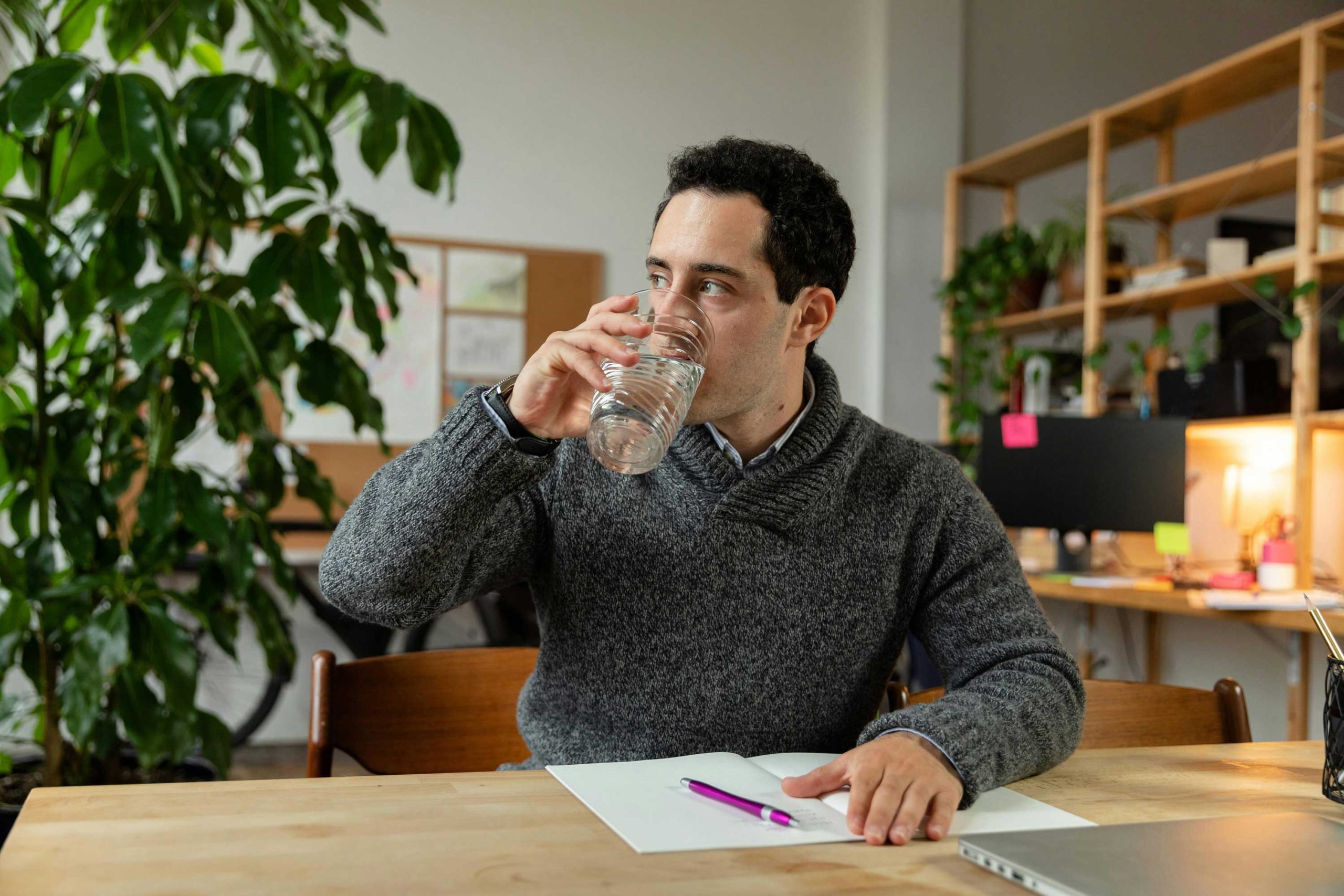 man sitting at desk sipping water from a glass